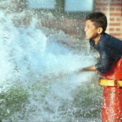 A young boy in the Logan Square neighborhood of Chicago, diverts water being released from a fire hydrant during a sweltering heat wave in the summer of 1998.